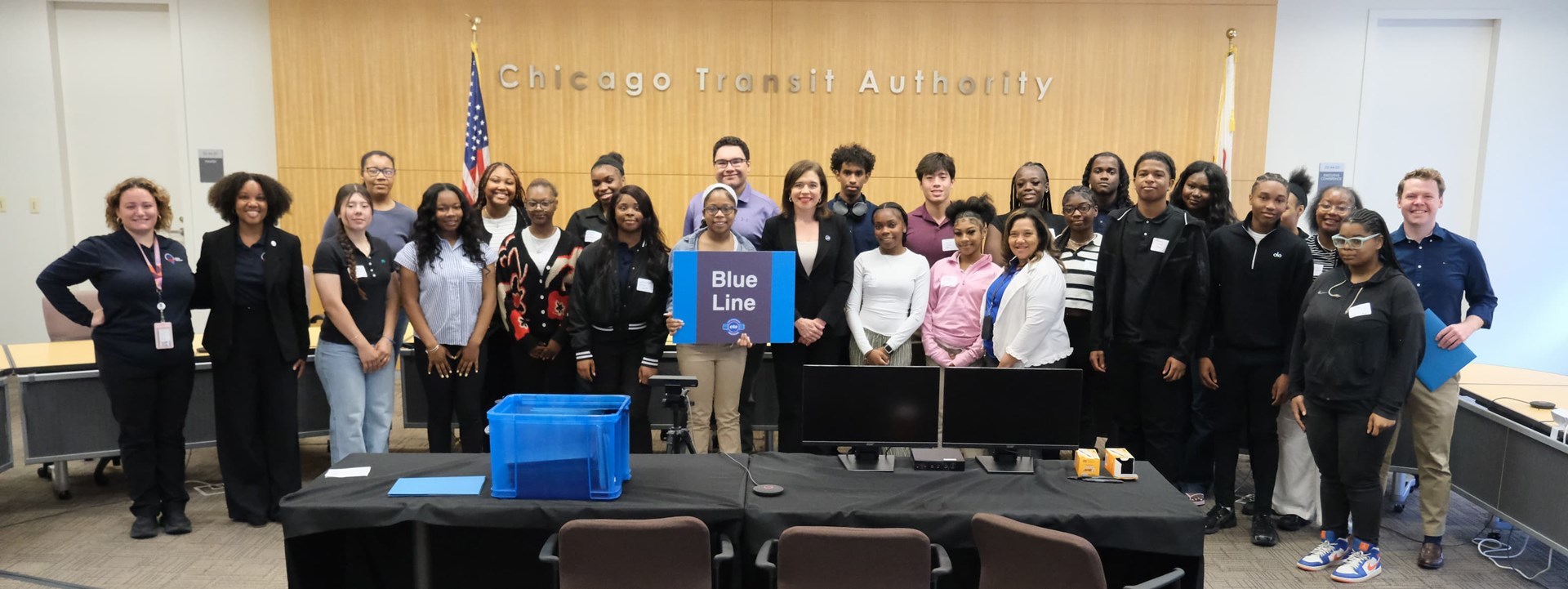 Interns posing in the CTA boardroom with the president. One holds a Blue Line sign.