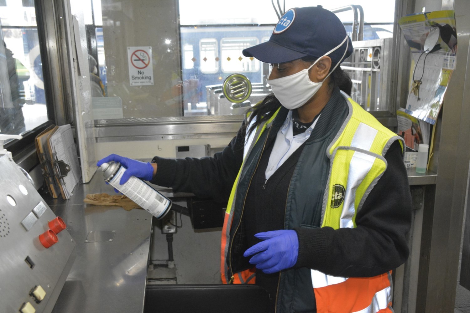 A rail station employee wears a mask and gloves as she disinfects her workspace at the start of her shift