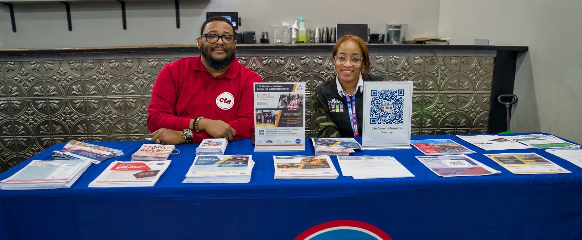 Two CTA employees sitting at a table with informational literature, ready to answer questions.
