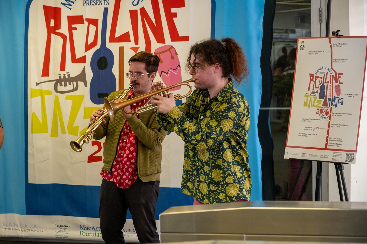 A saxophone player and a trumpet player in front of a Red Line Jazz poster.