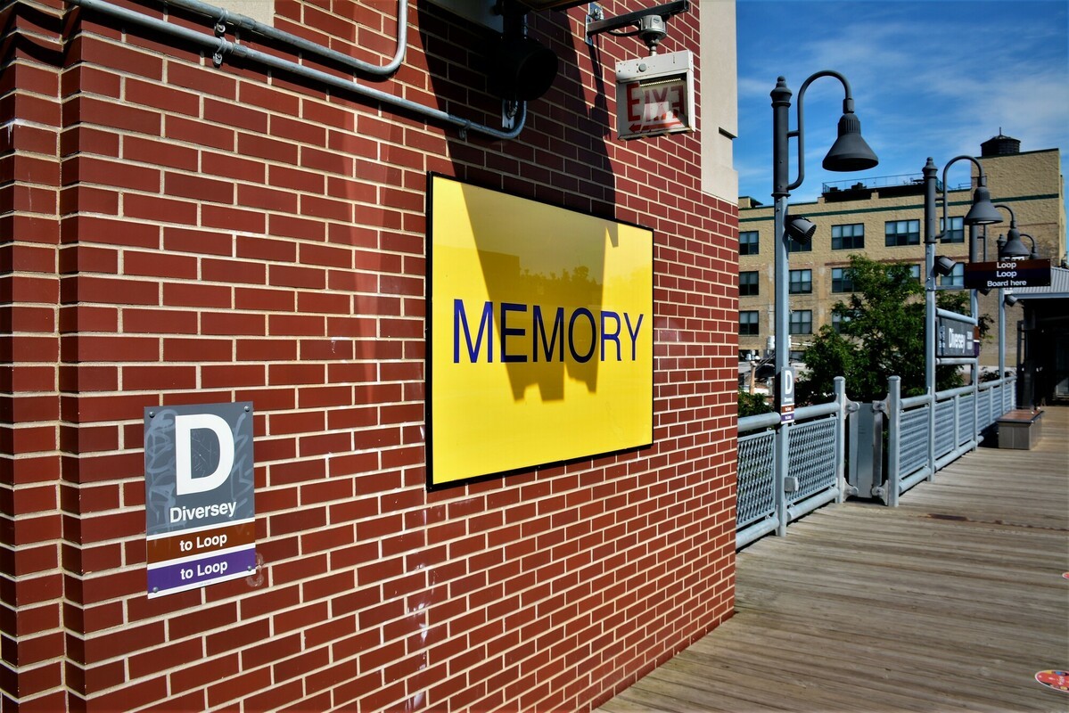 A bright yellow sign with blue letters spelling "MEMORY" featured on the platform of the Diversey station as part of the "Ordinary Relic" art installation.