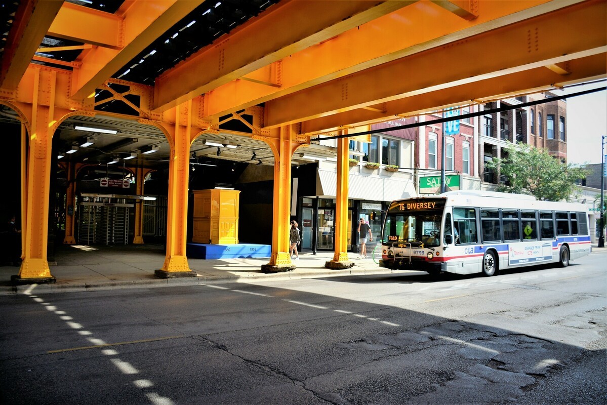 A CTA bus driving under the Diversey elevated structure which has been painted bright yellow as one of the component of the new art installation.