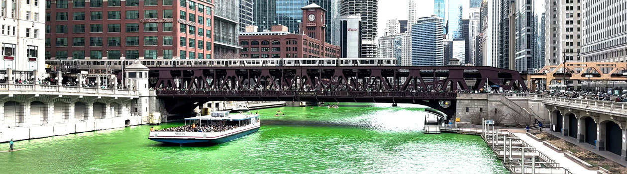 L train on a bridge over the river dyed green.