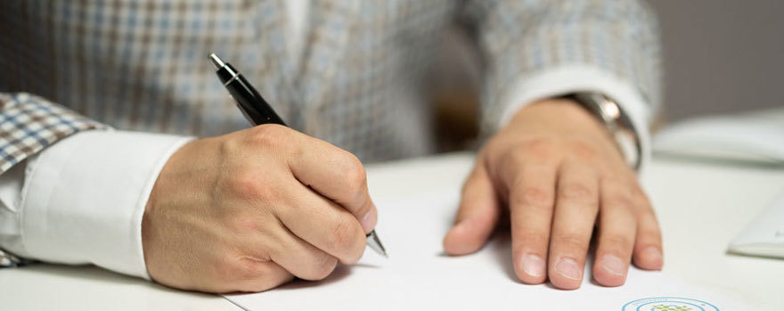 Close up of hands and arms in business attire working on a document with a pen